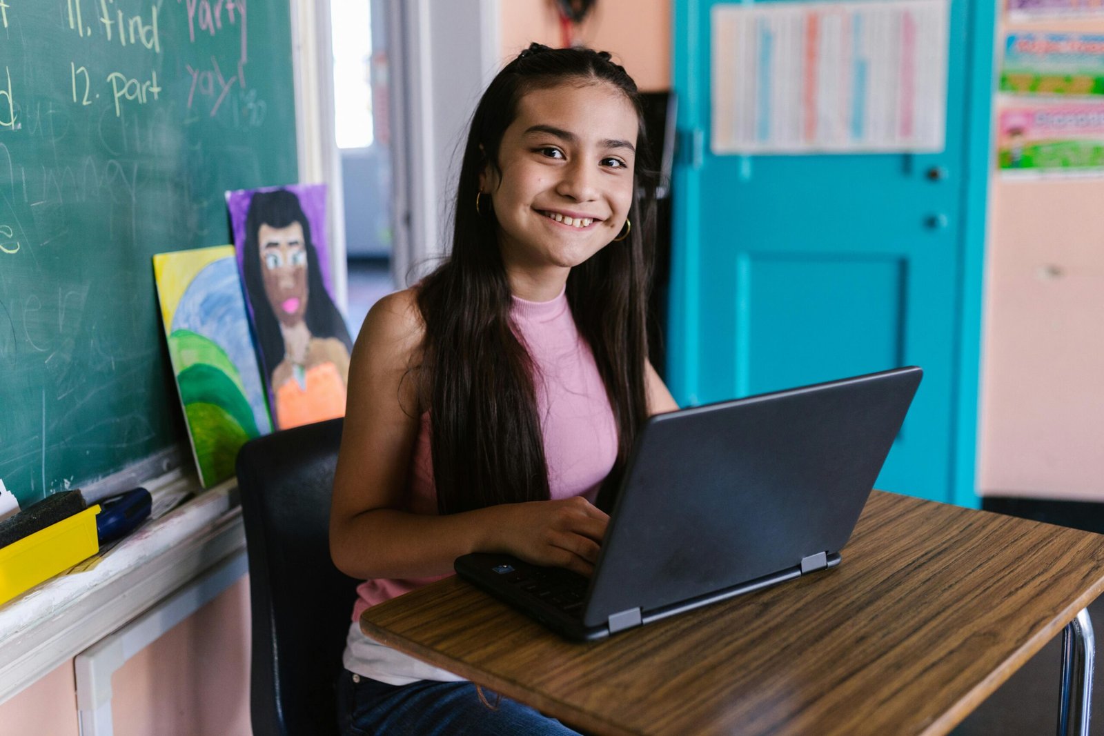 Young student smiling while using a laptop in a classroom setting.